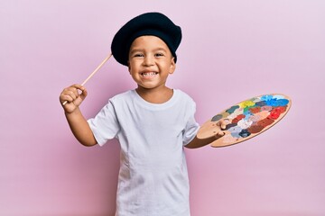 Adorable latin toddler smiling happy wearing artist style using paintbrush and palette over...
