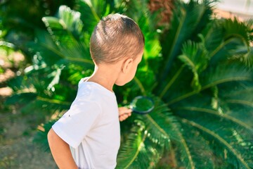 Adorable hispanic boy using magnifying glass playing at the park.