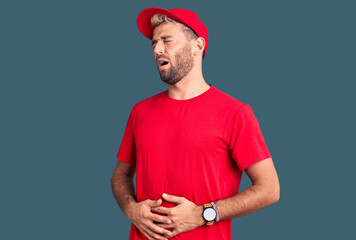 Young handsome blond man wearing t-shirt and cap with hand on stomach because nausea, painful disease feeling unwell. ache concept.