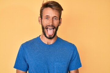 Handsome caucasian man with beard wearing casual clothes sticking tongue out happy with funny expression. emotion concept.