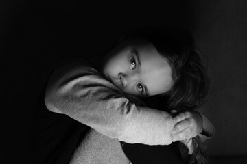 Black and white photo of a sad girl looking forward head on her knees
