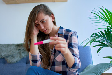 Portrait of sad pensive woman holding head and looking at pregnancy test result