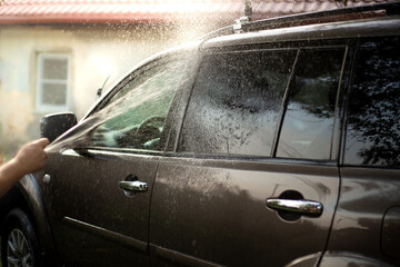 a man with a hose washes the car in the courtyard of the house, a stream of water is sprayed on the glass.