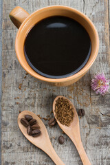 Black coffee in a cup and coffee beans in a wooden spoon on a wooden table.