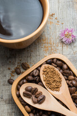 Black coffee in a cup and coffee beans in a wooden spoon on a wooden table.