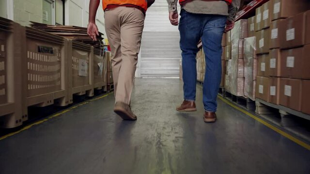 Two male colleagues walking with purpose to collect delivered parcels at entrance of factory shop in warehouse. 