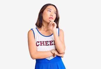 Young beautiful chinese girl wearing cheerleader uniform with hand on chin thinking about question,...