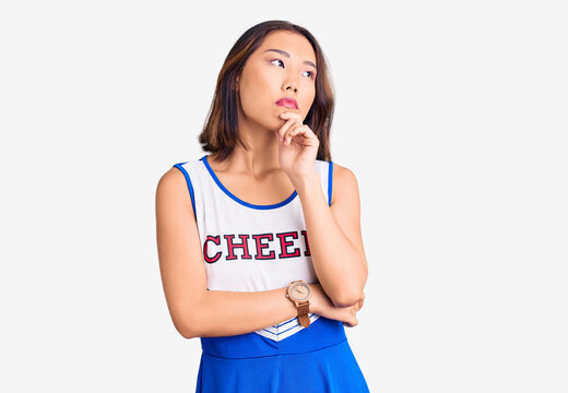Young beautiful chinese girl wearing cheerleader uniform with hand on chin thinking about question, pensive expression. smiling with thoughtful face. doubt concept.