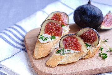 Close view of two sandwiches with goat cheese, fig and thyme on fresh crispy bread served on a wooden plate on light grey back