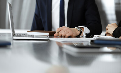 Unknown businessmen and woman sitting, using laptop computer and discussing questions at meeting in modern office, close-up