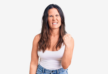Young beautiful brunette woman wearing casual sleeveless t-shirt angry and mad raising fist...