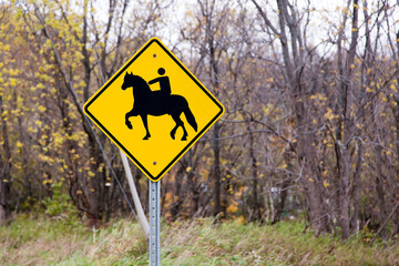 Horseback riding roadside warning sign seen in rural area in the Fall, with wooded area in soft focus background, Quebec City, Quebec, Canada