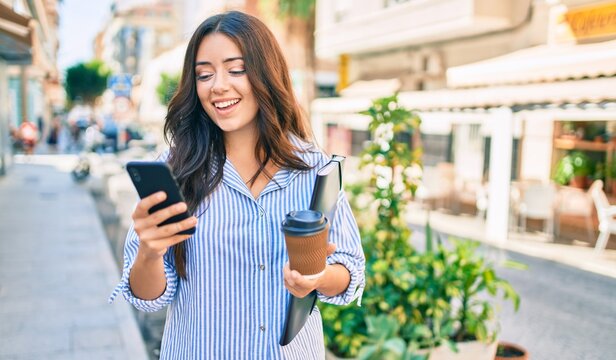Young hispanic businesswoman using smartphone and drinking take away coffee at the city.