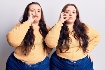 Young plus size twins wearing casual clothes mouth and lips shut as zip with fingers. secret and...