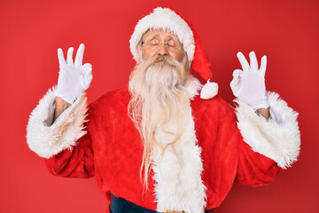 Old senior man with grey hair and long beard wearing traditional santa claus costume relax and...