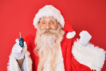 Old senior man with grey hair and long beard wearing santa claus costume holding car keys screaming proud, celebrating victory and success very excited with raised arm