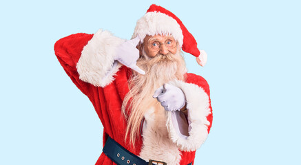 Old senior man with grey hair and long beard wearing traditional santa claus costume smiling doing talking on the telephone gesture and pointing to you. call me.