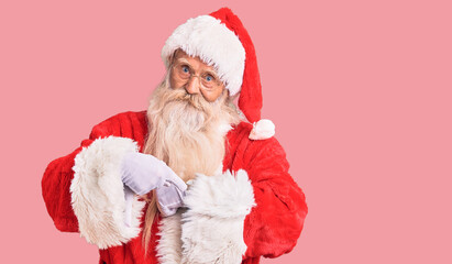 Old senior man with grey hair and long beard wearing traditional santa claus costume in hurry pointing to watch time, impatience, upset and angry for deadline delay
