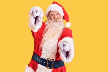 Old senior man with grey hair and long beard wearing traditional santa claus costume pointing to you and the camera with fingers, smiling positive and cheerful