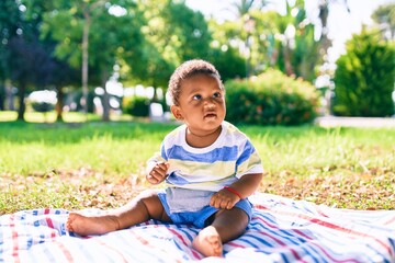 Adorable african american toddler sitting on the grass at the park.