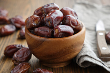 Wooden bowl of dates fruits and knife on wooden kitchen table.