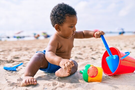 Adorable african american toddler playing with toys sitting on the sand at the beach.