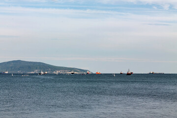 Small sailing yachts and ships queuing up for unloading at the seaport at the exit from the sea bay.