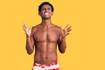 Fototapeta premium African handsome man wearing swimsuit and sunglasses celebrating mad and crazy for success with arms raised and closed eyes screaming excited. winner concept