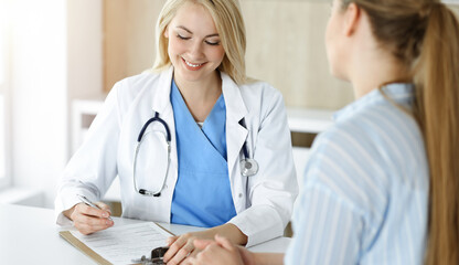 Woman-doctor and patient sitting and talking in sunny clinic. Blonde therapist is cheerfully smiling