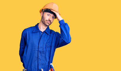 Young hispanic man wearing worker uniform surprised with hand on head for mistake, remember error. forgot, bad memory concept.