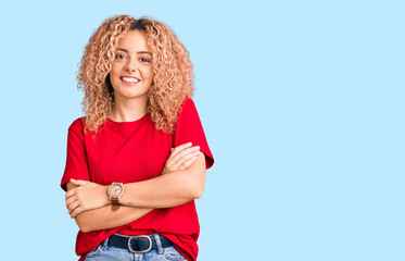 Young blonde woman with curly hair wearing casual red tshirt happy face smiling with crossed arms looking at the camera. positive person.