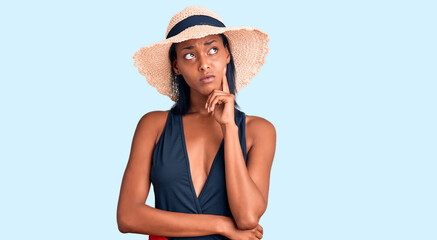 Young african american woman wearing swimsuit and summer hat with hand on chin thinking about question, pensive expression. smiling with thoughtful face. doubt concept.