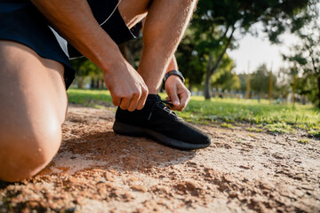 Young male athlete bending down tying running shoes before exercising on outdoor running path