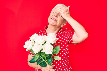 Senior beautiful woman with blue eyes and grey hair holding bouquet of white flowers stressed and frustrated with hand on head, surprised and angry face