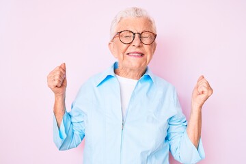 Senior beautiful woman with blue eyes and grey hair wearing glasses very happy and excited doing winner gesture with arms raised, smiling and screaming for success. celebration concept.
