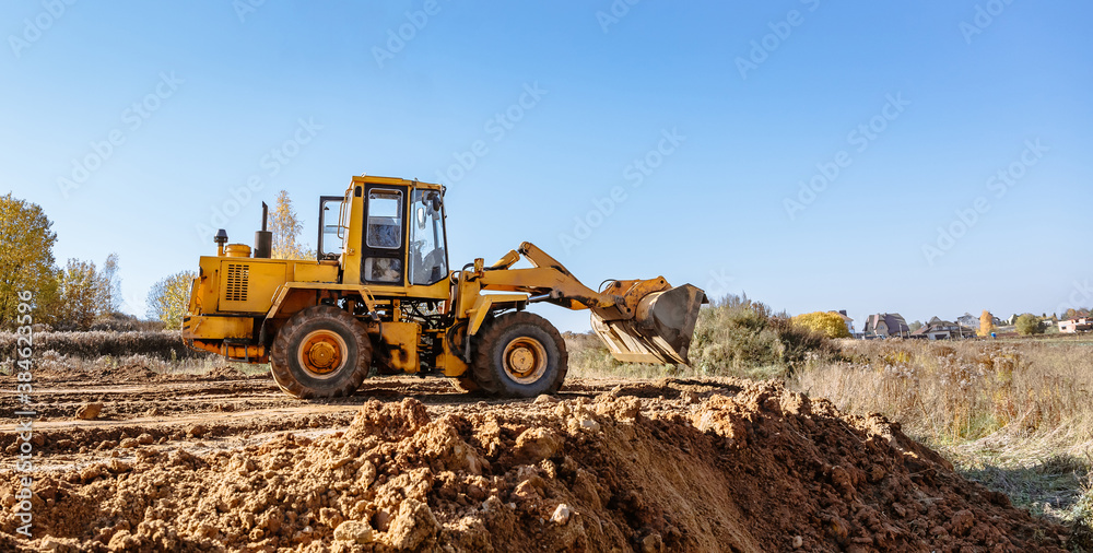 Wall mural large yellow wheel loader aligns a piece of land for a new building. preparation of the land for the