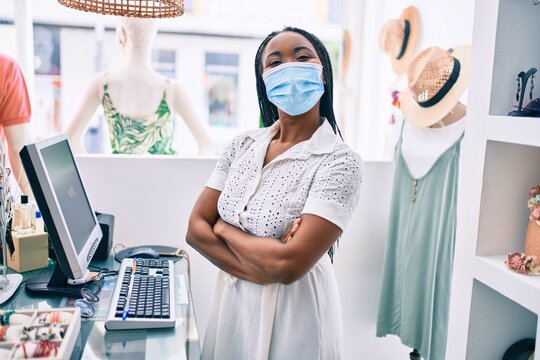 Young african american shopkeeper woman wearing medical mask working at clothing store