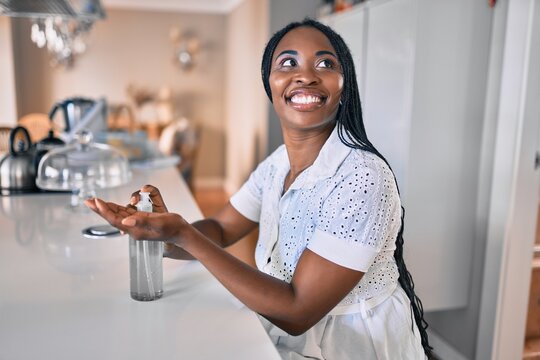 Young african american woman smiling happy using sanitizer hand gel at home