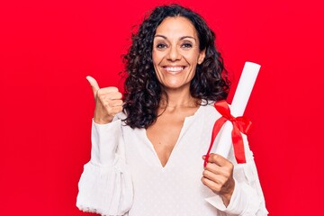 Middle age beautiful woman holding graduate degree diploma smiling happy and positive, thumb up doing excellent and approval sign - obrazy, fototapety, plakaty