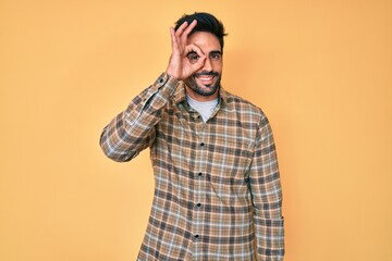 Handsome hispanic man with beard wearing casual clothes doing ok gesture with hand smiling, eye looking through fingers with happy face.