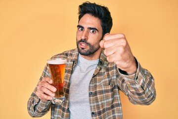 Handsome hispanic man with beard drinking a pint of beer annoyed and frustrated shouting with anger, yelling crazy with anger and hand raised