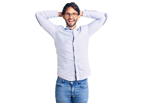 Handsome hispanic man wearing business shirt and glasses relaxing and stretching, arms and hands behind head and neck smiling happy