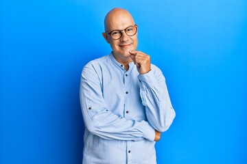 Middle age bald man wearing casual clothes and glasses looking confident at the camera with smile with crossed arms and hand raised on chin. thinking positive.