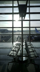 Empty seats at the airport.
Two rows of empty seats at the airport against the backdrop of a large window. in the background a runway with airplanes.