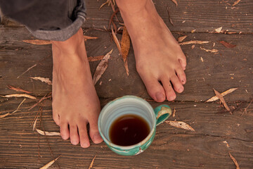Women's bare feet stand on a wooden floor covered with autumn leaves.