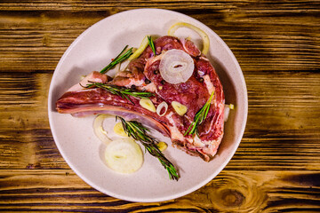 Raw ribeye steak, spices, rosemary, onion and garlic in a ceramic plate on wooden table. Top view
