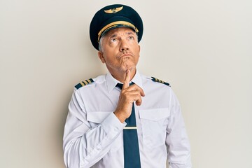Handsome middle age mature man wearing airplane pilot uniform thinking concentrated about doubt with finger on chin and looking up wondering