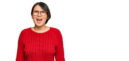 Young beautiful hispanic woman with short hair wearing casual sweater and glasses angry and mad screaming frustrated and furious, shouting with anger. rage and aggressive concept.