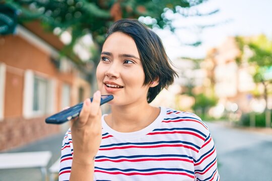 Young latin girl smiling happy sending voice message using smartphone at the city