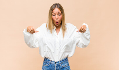 young pretty woman feeling shocked, open-mouthed and amazed, looking and pointing downwards in disbelief and surprise © kues1